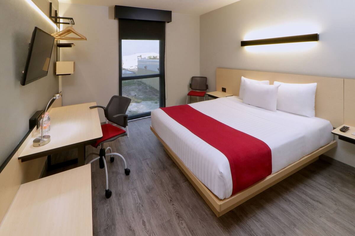 Een hotelkamer met een bed, bureau, stoel en een televisie aan de muur.