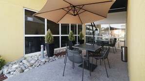 An outdoor patio with a table and chairs, a large umbrella, potted plants, and a view of the street. - City Express by Marriott Piedras Negras (Piedras Negras)