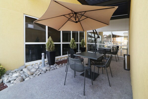 An outdoor patio with a table and chairs, a large umbrella, and potted plants. - City Express by Marriott Piedras Negras (Piedras Negras)