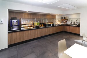 Un área de cocina moderna con una estación de café integrada, microondas y diversos utensilios para preparar alimentos.