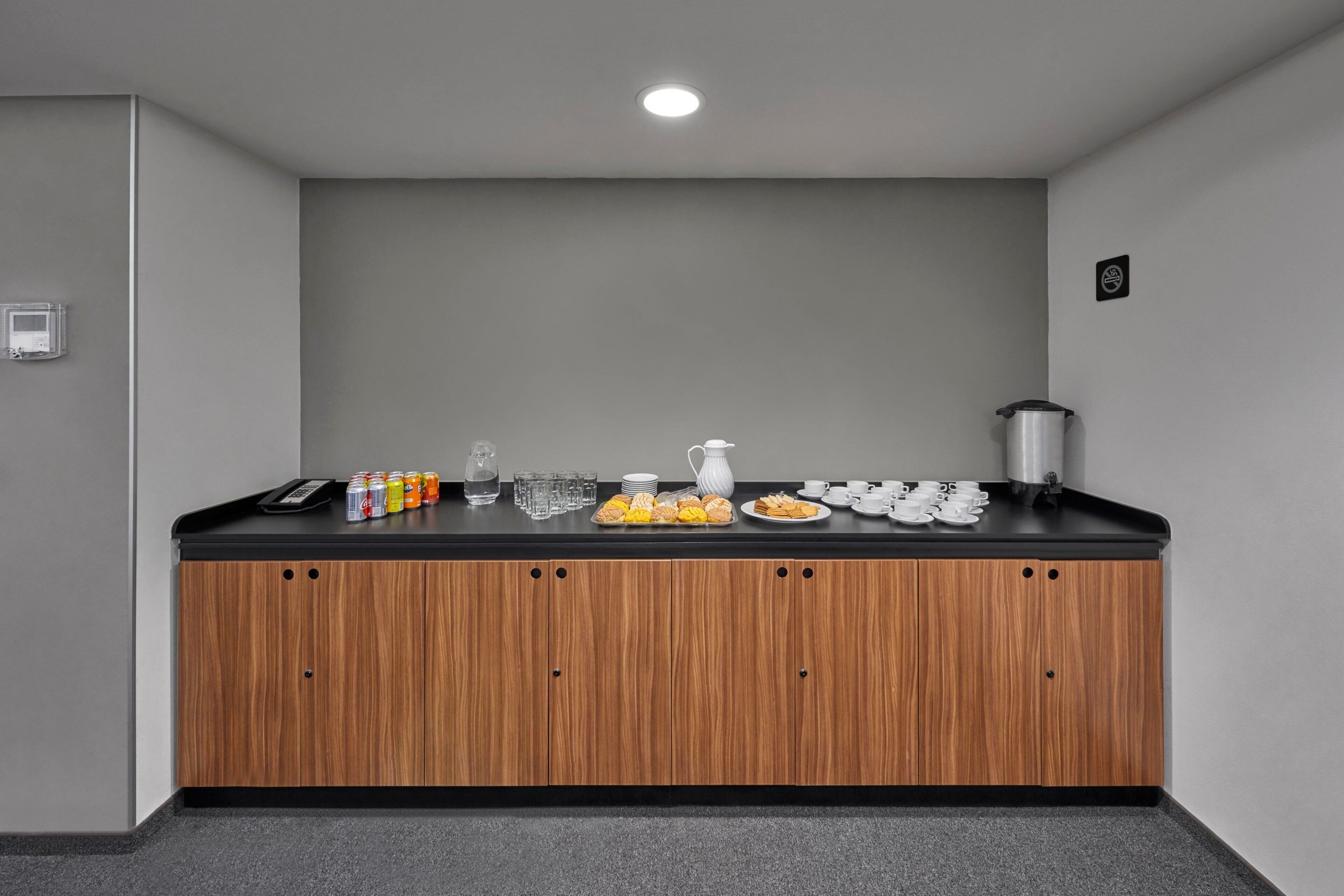 A kitchenette with a black countertop, wooden cabinets, a coffee maker, and various food items.