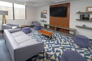 A modern lounge area with a sofa, armchairs, a coffee table, and a TV mounted on a brick wall.