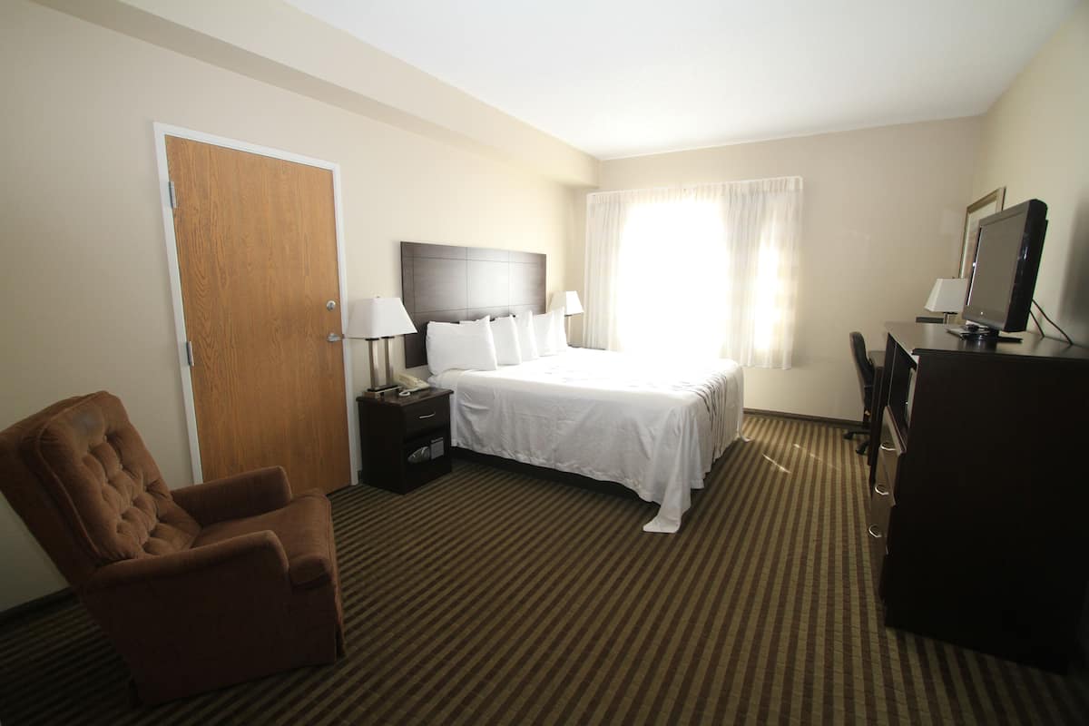 A hotel room with a bed, a chair, a desk with a computer, and a television.