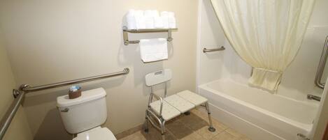 A bathroom with a toilet, a shower with a curtain, a grab bar, and a shelf with towels.