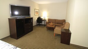 Ein Hotelzimmer mit Flachbildfernseher auf einem Standfuß, einer Couch, einem kleinen Tisch und einem Schreibtisch mit Stuhl.