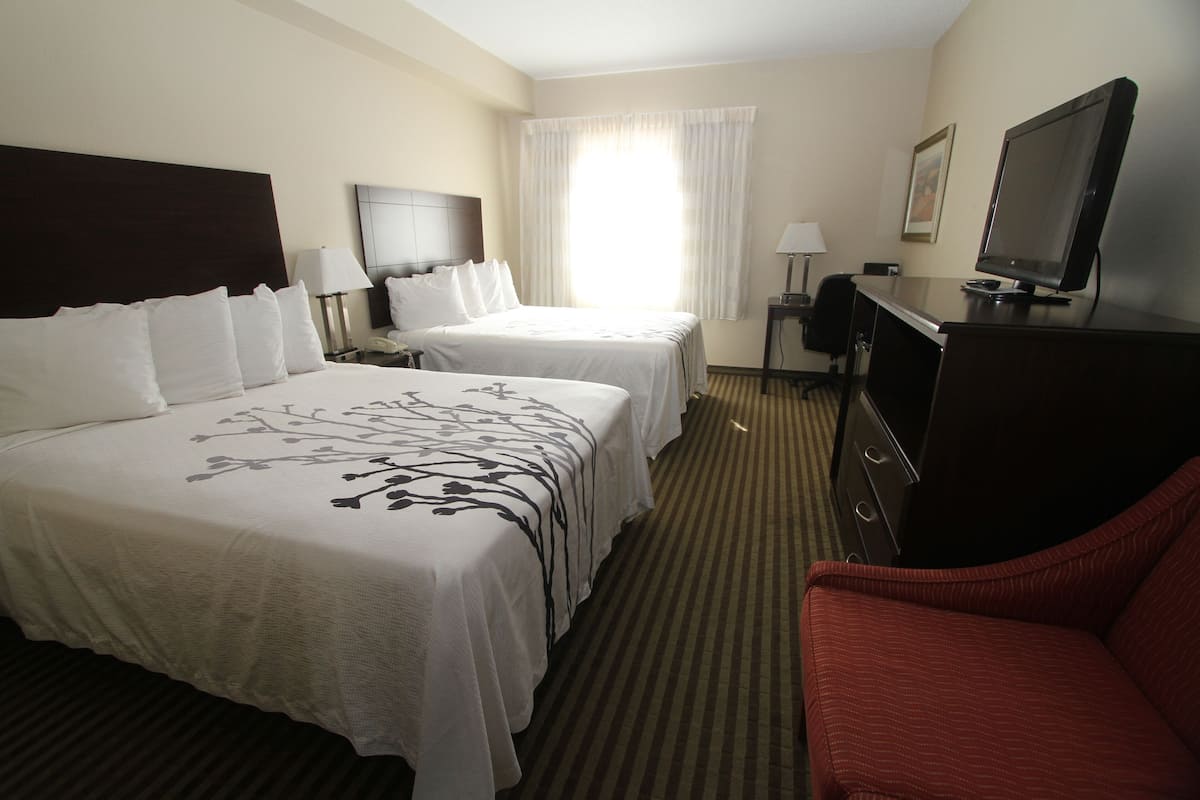 A hotel room with two beds, a desk with a computer, a TV, and a red chair.