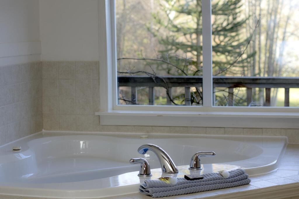 A bathroom with a bathtub, two faucets, and a window with a view of trees.