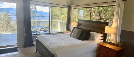 Ein Schlafzimmer mit einem großen Bett, einem Nachttisch mit Lampe und Blick ins Freie von einem Balkon aus.