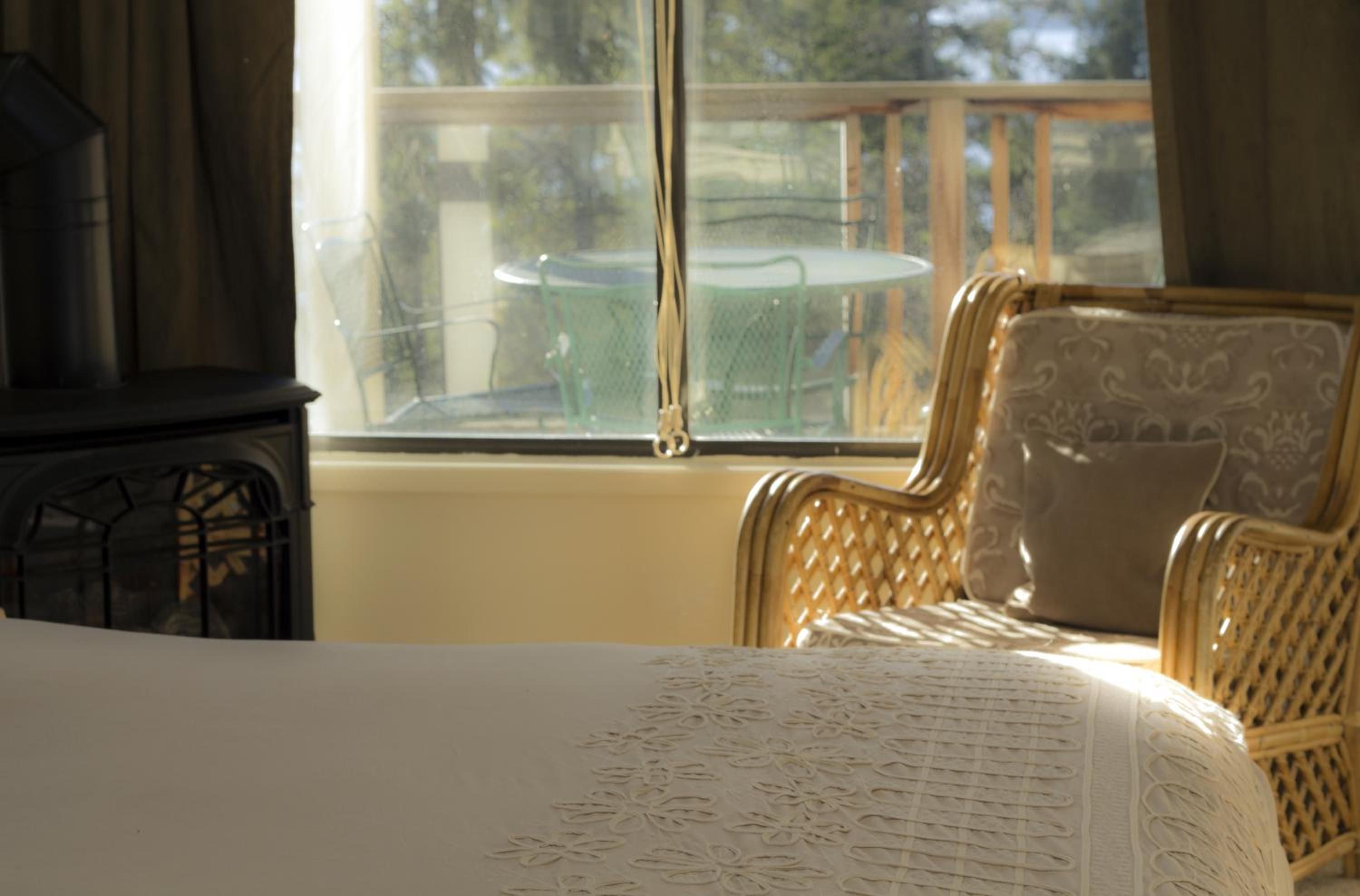 A room with a bed, a wicker chair, and a view through a window.