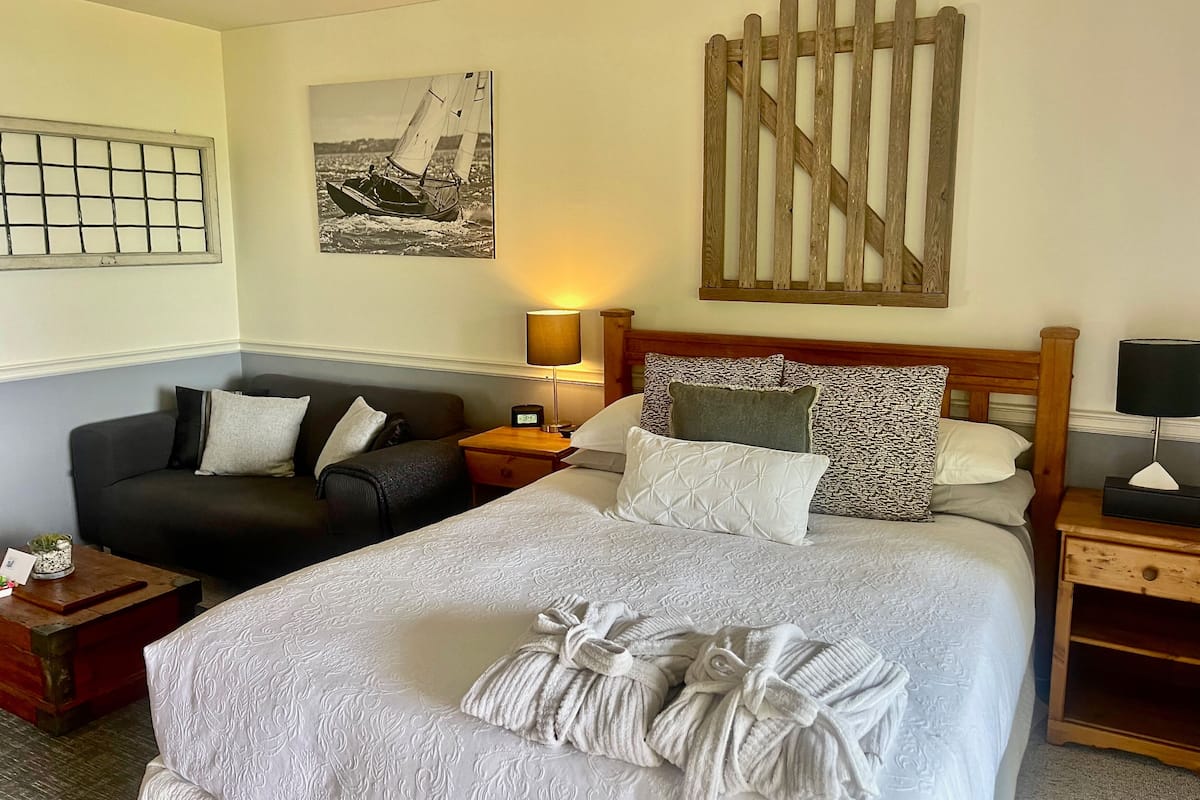 Ein Hotelzimmer mit einem großen Bett, einem Sofa, einem hölzernen Kopfteil, einem Nachttisch und einem an der Wand befestigten Bild von einem Segelboot.