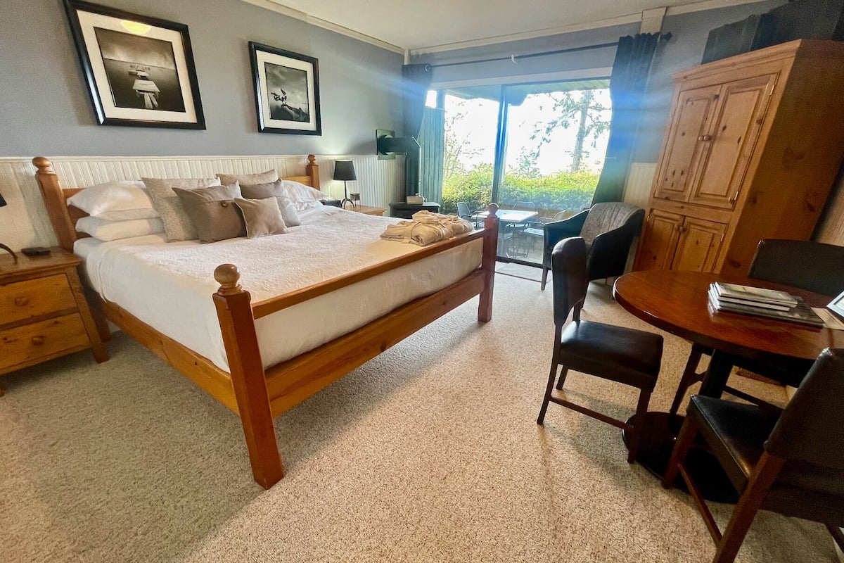Ein Schlafzimmer mit einem großen Bett, einem Holznachttisch, einem Schreibtisch mit Stuhl und einem Kleiderschrank. An der Wand hängen zwei gerahmte Bilder.