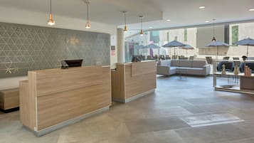 Un área de recepción moderna con un mostrador de madera, una zona de estar con sofá y ventanas amplias que dejan entrar luz natural.
