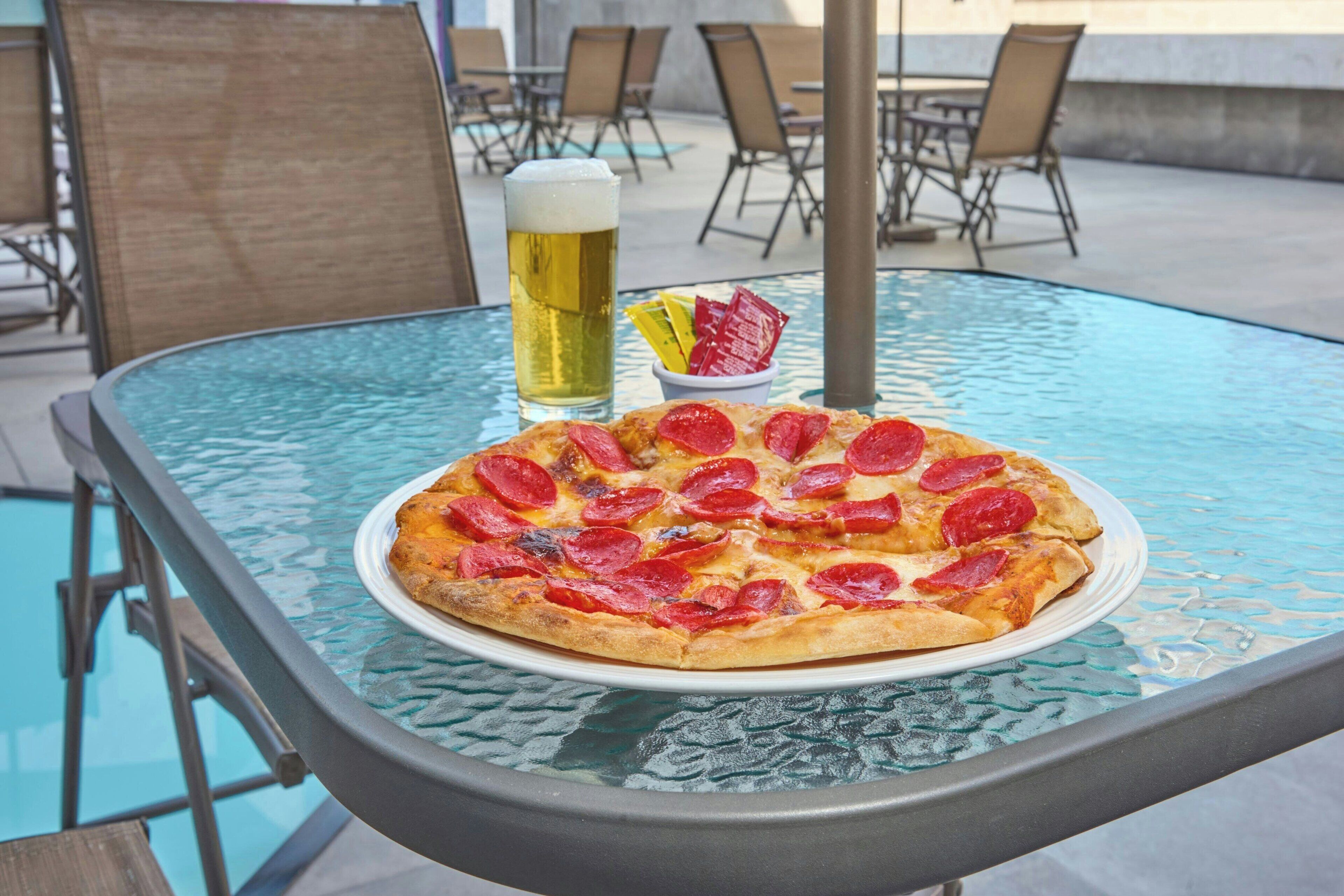 Una mesa de vidrio con una pizza y una cerveza encima.