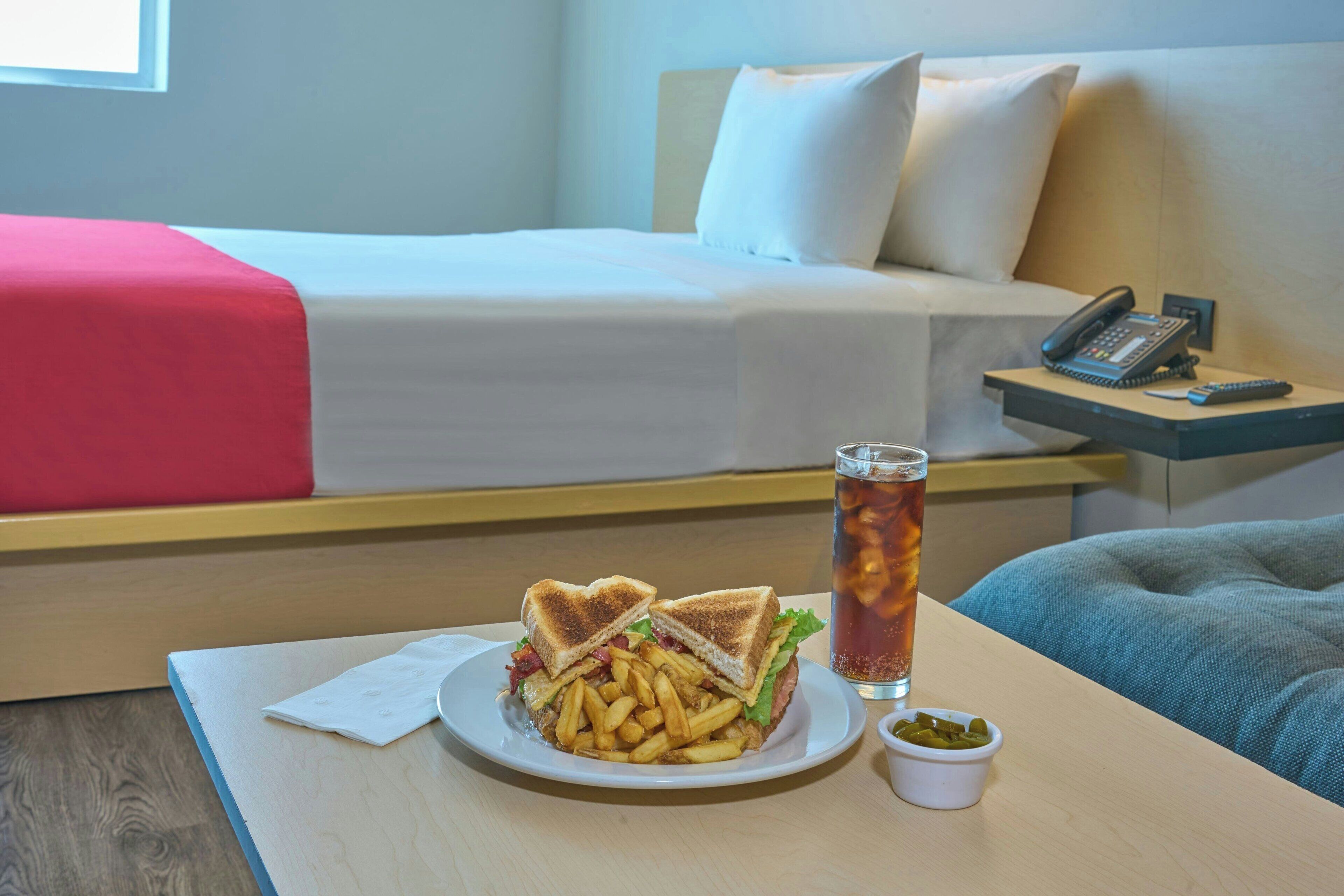 Una habitación de hotel con una cama, una mesita de noche con un teléfono, un plato de comida y una bebida.