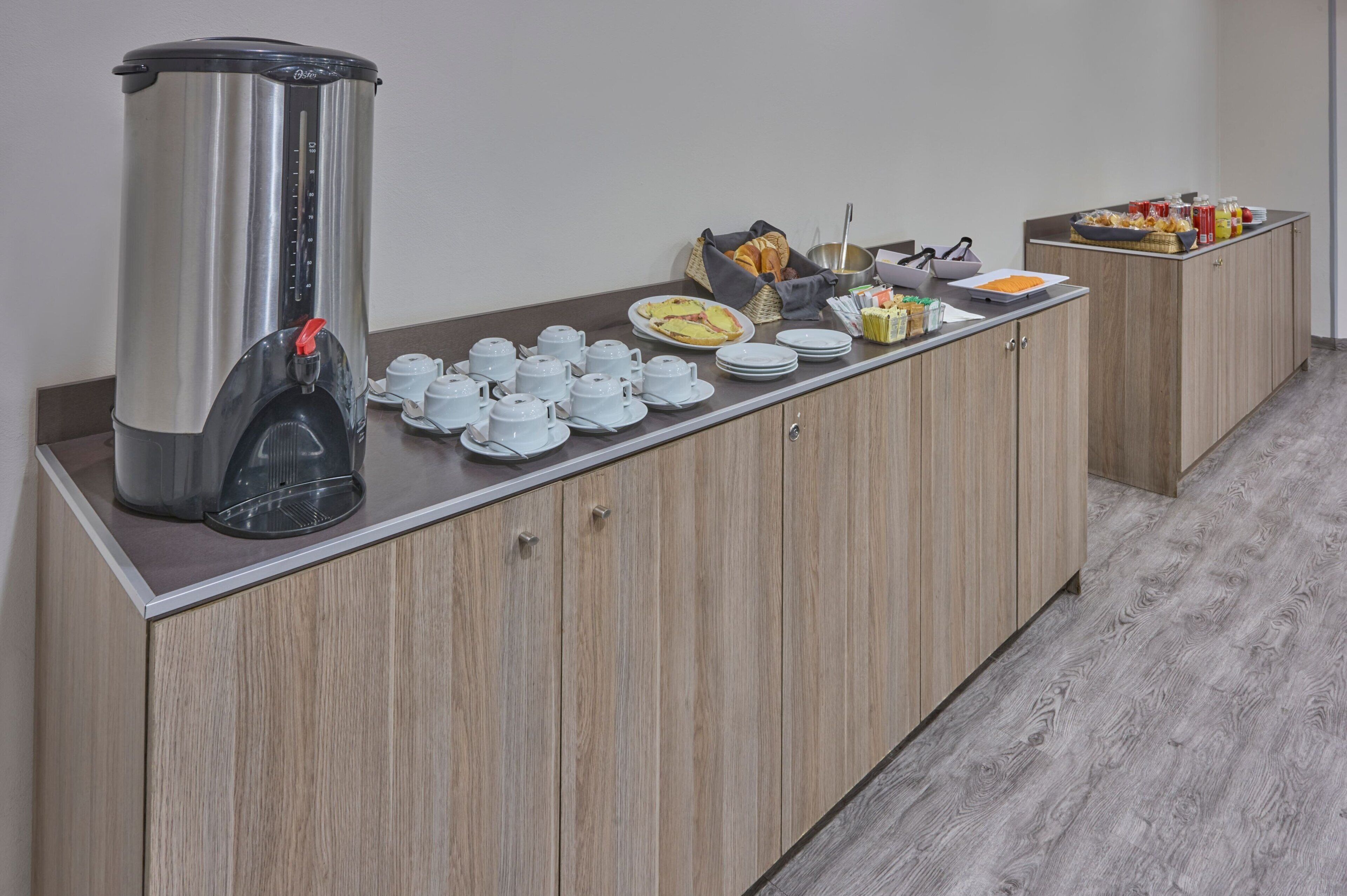 A breakfast buffet setup with a coffee maker, tea pots, and various food items on a wooden counter.