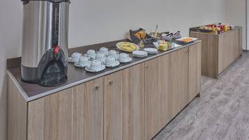A breakfast buffet setup with a coffee maker, tea pots, and various food items on a wooden counter.
