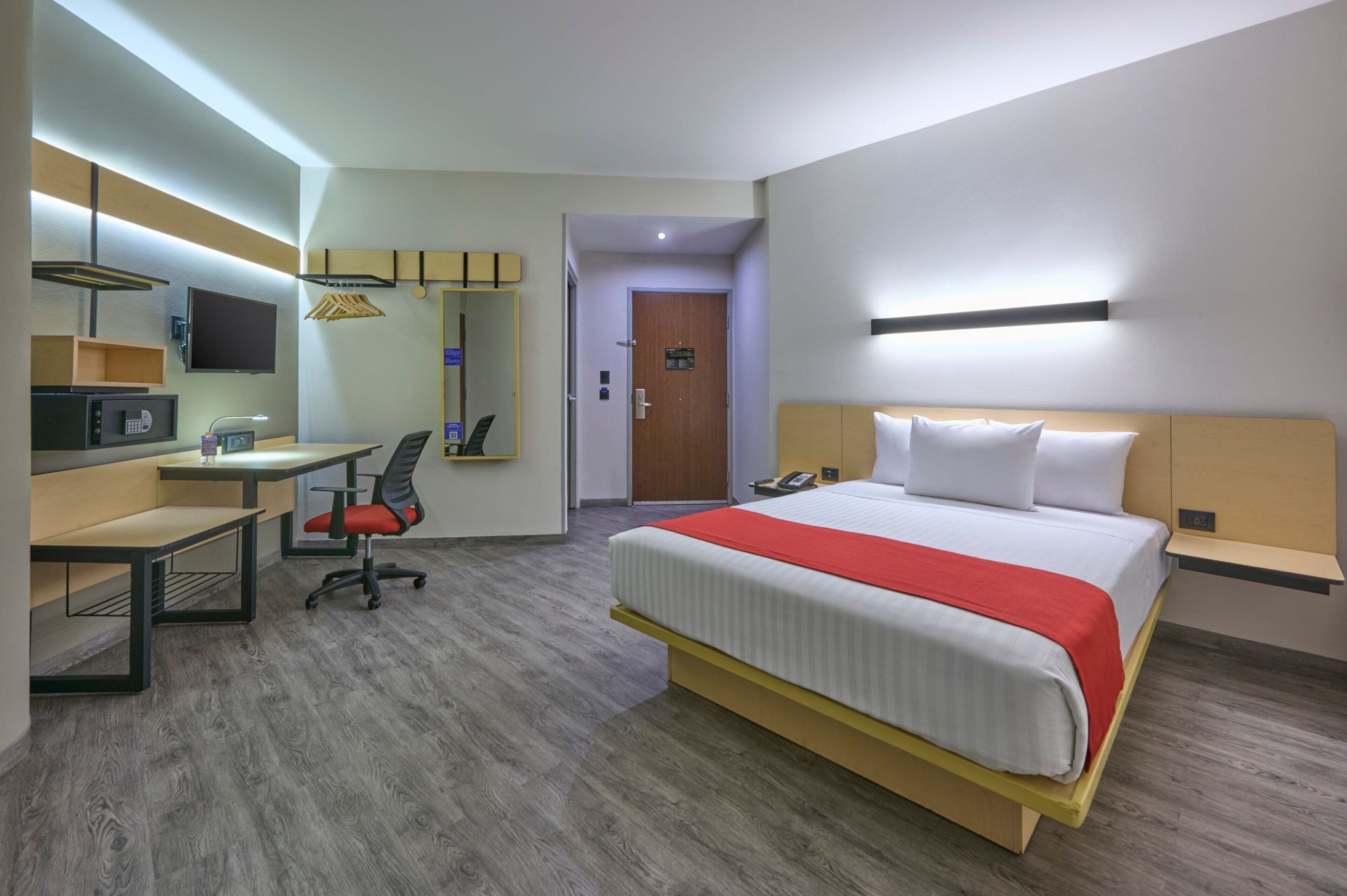 A hotel room with a bed, desk, chair, and a television.