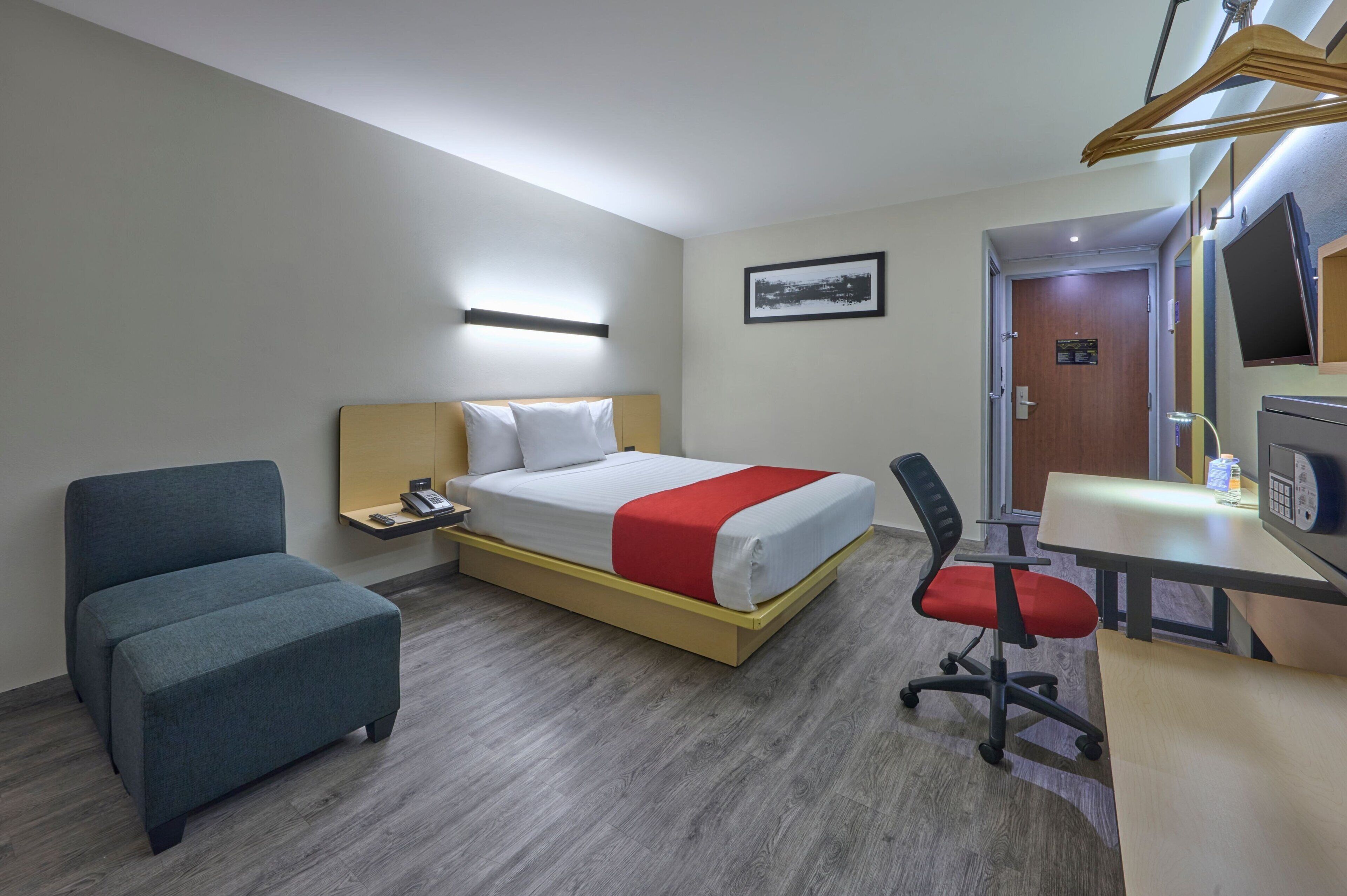Habitación de hotel con cama, escritorio, sillón, mesa de noche, teléfono y televisor.