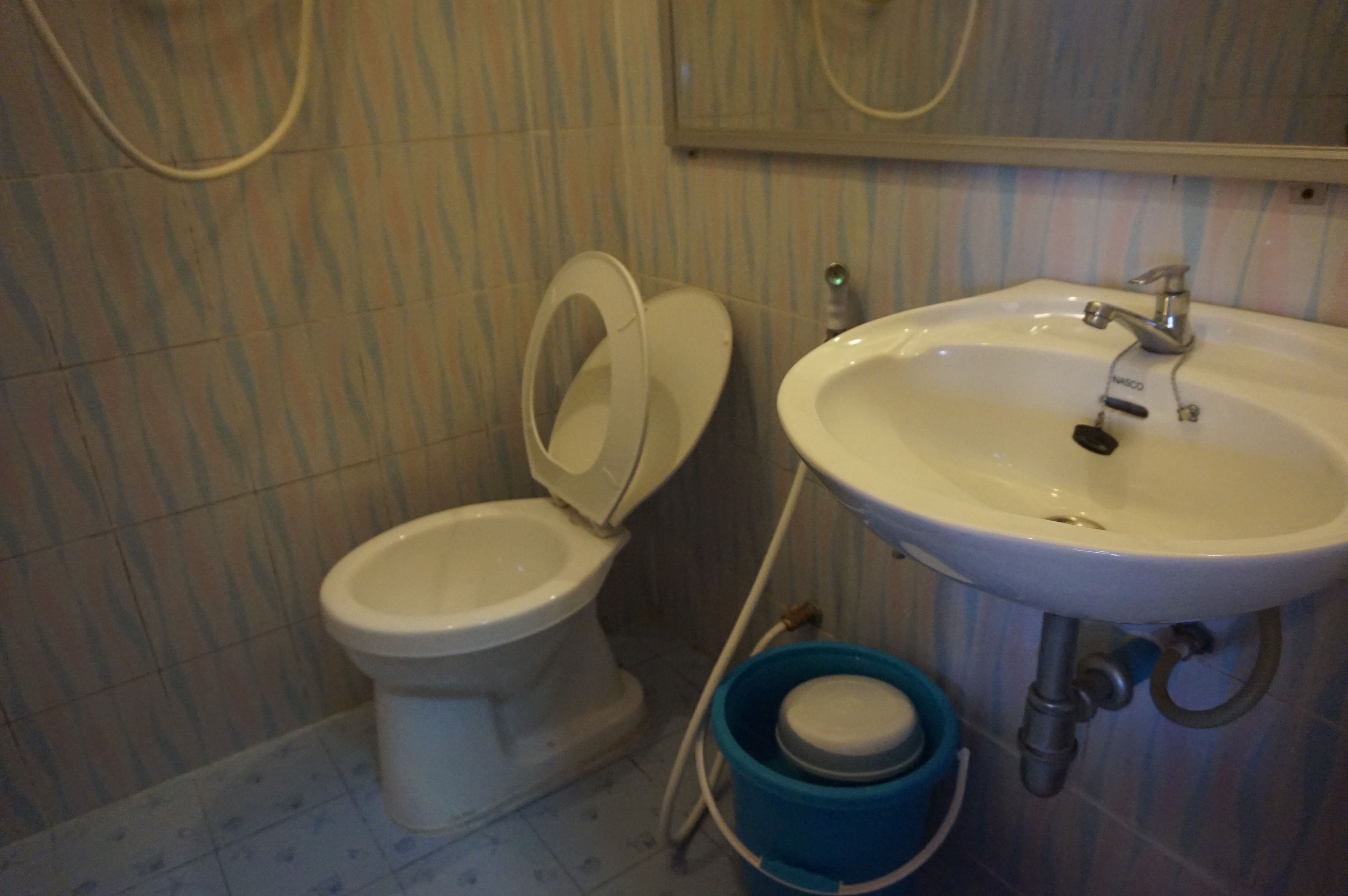 Un baño con un inodoro, un lavamanos y un cubo azul.