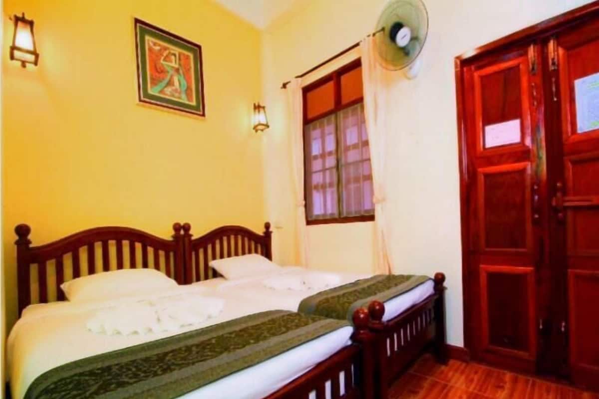 Una habitación con dos camas de madera, una ventana con cortinas, un ventilador en la pared y una puerta con un cartel.