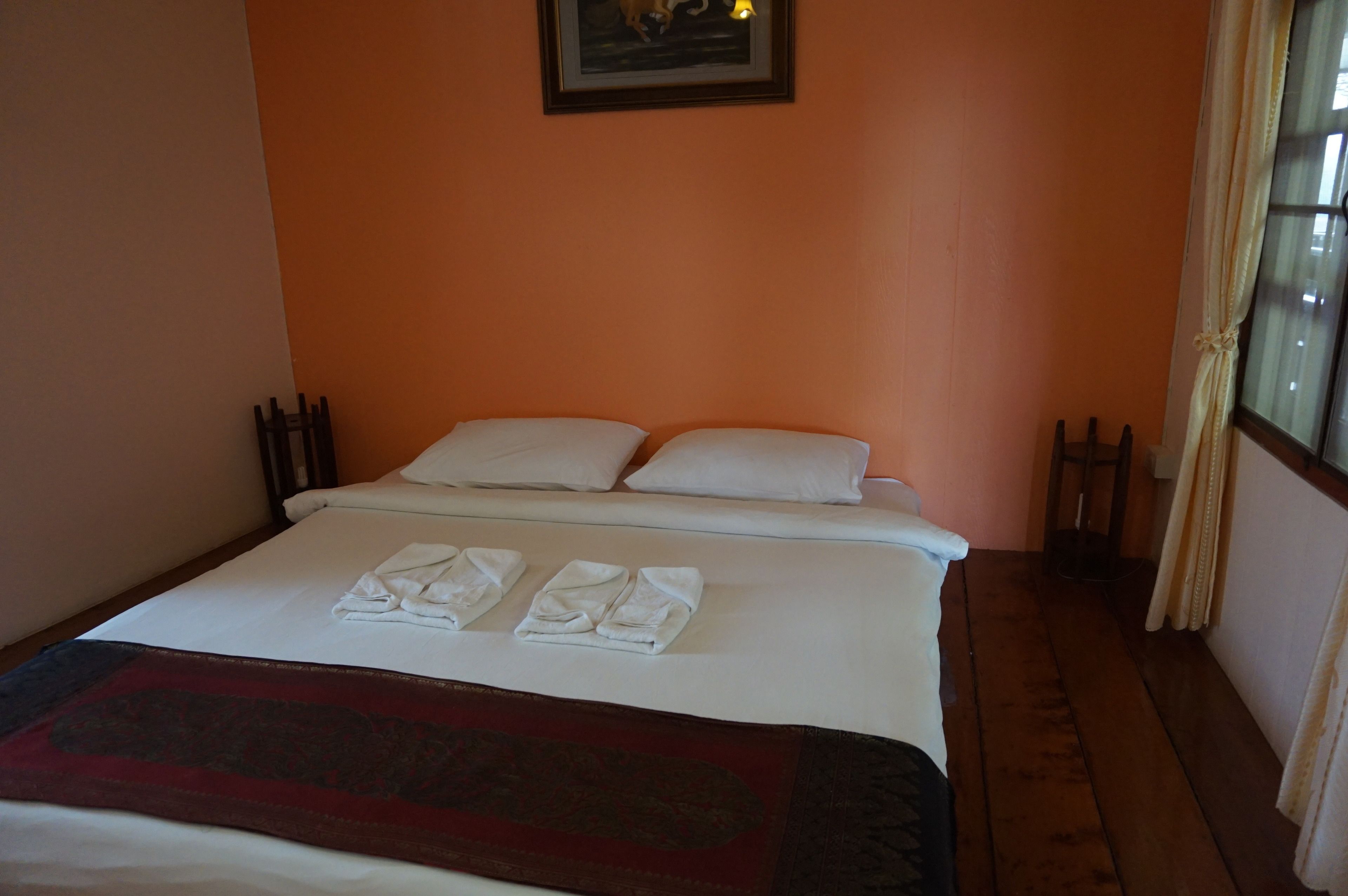 A neatly made bed with white linens and towels, a dark red throw blanket, and a framed picture on the wall.