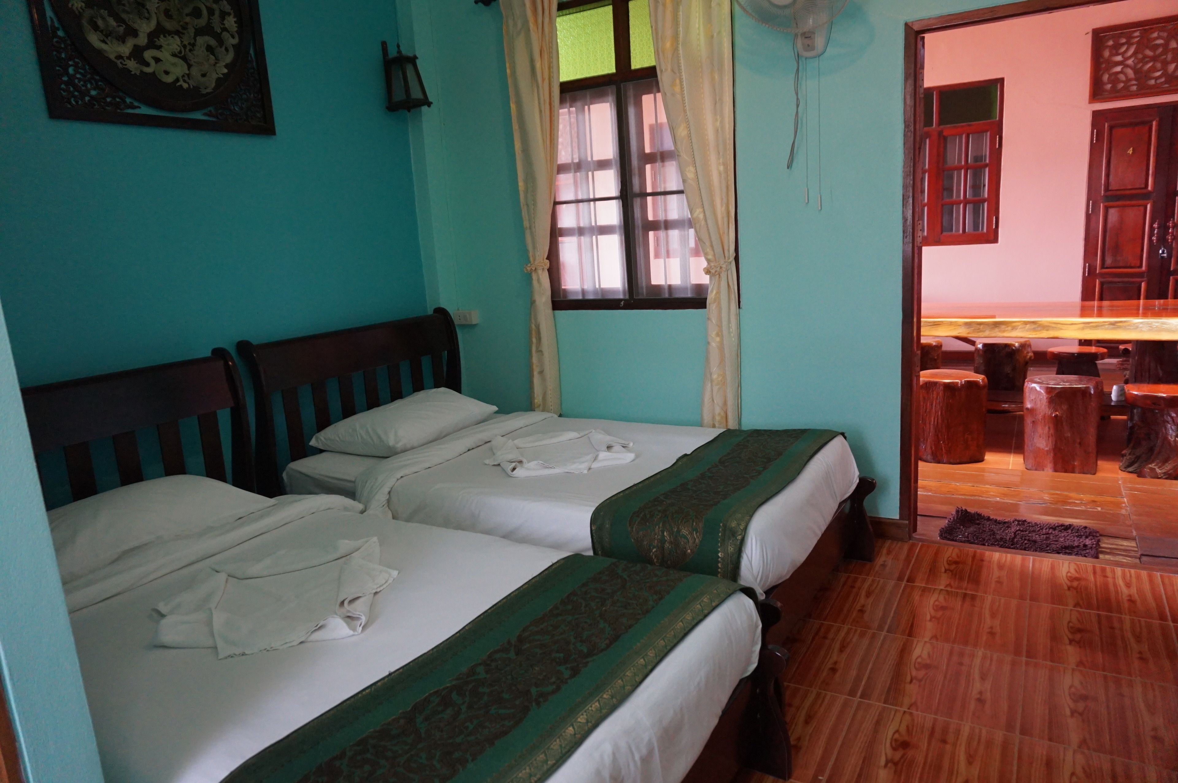 A room with two beds, a wooden headboard, a window with curtains, and a wooden dining table with stools.