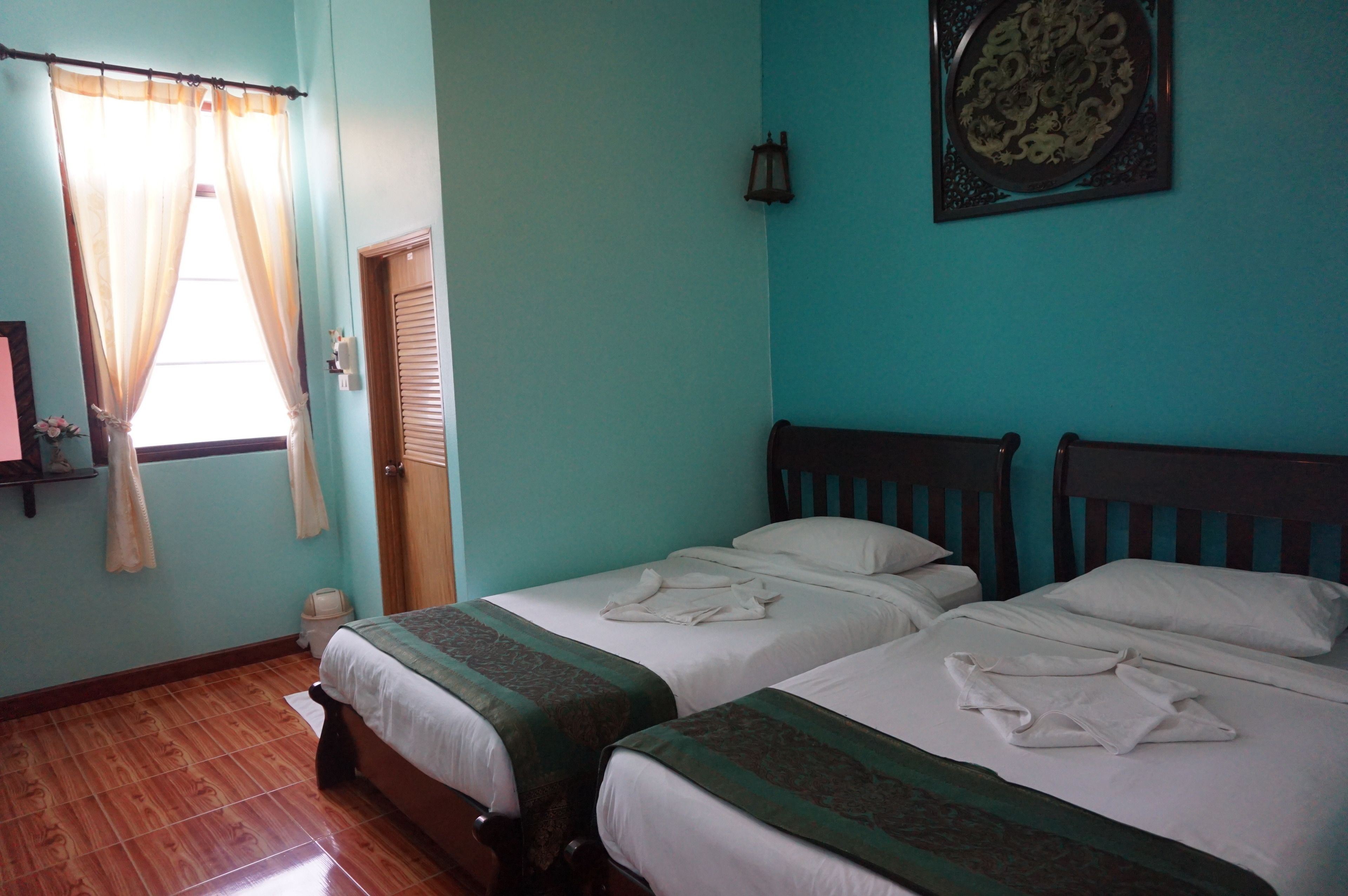 Una habitación con dos camas, una ventana con cortinas, una puerta, una lámpara de pared y un plato decorativo.