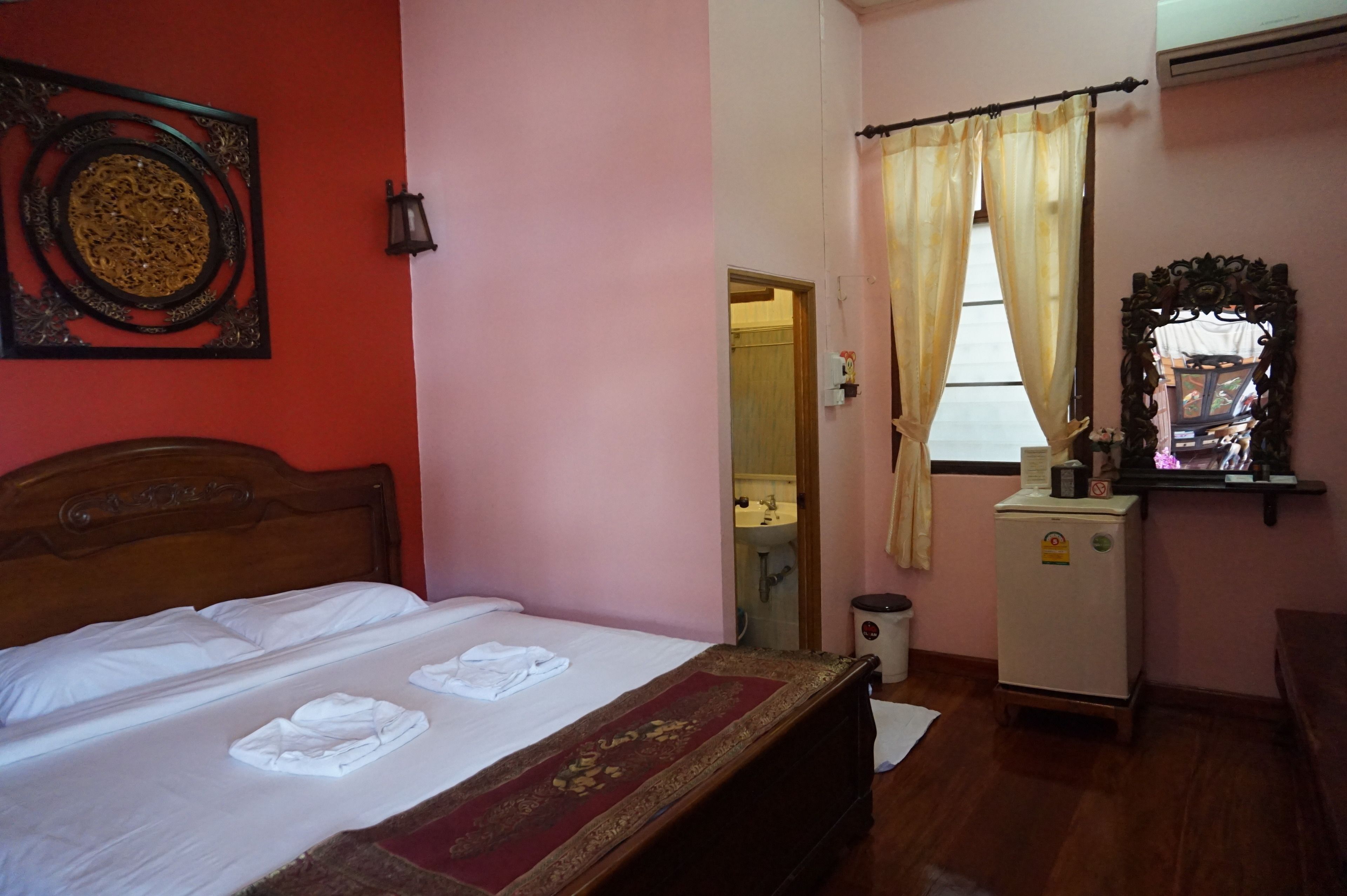 Une chambre d’hôtel avec un lit, un petit réfrigérateur, un miroir et une fenêtre avec des rideaux.