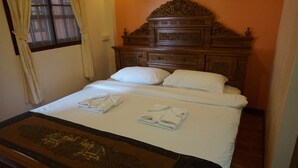 Een net opgemaakt bed met witte lakens en handdoeken, een houten hoofdbord met gedetailleerde houtsnijwerken, en een bedloper met een patroon.