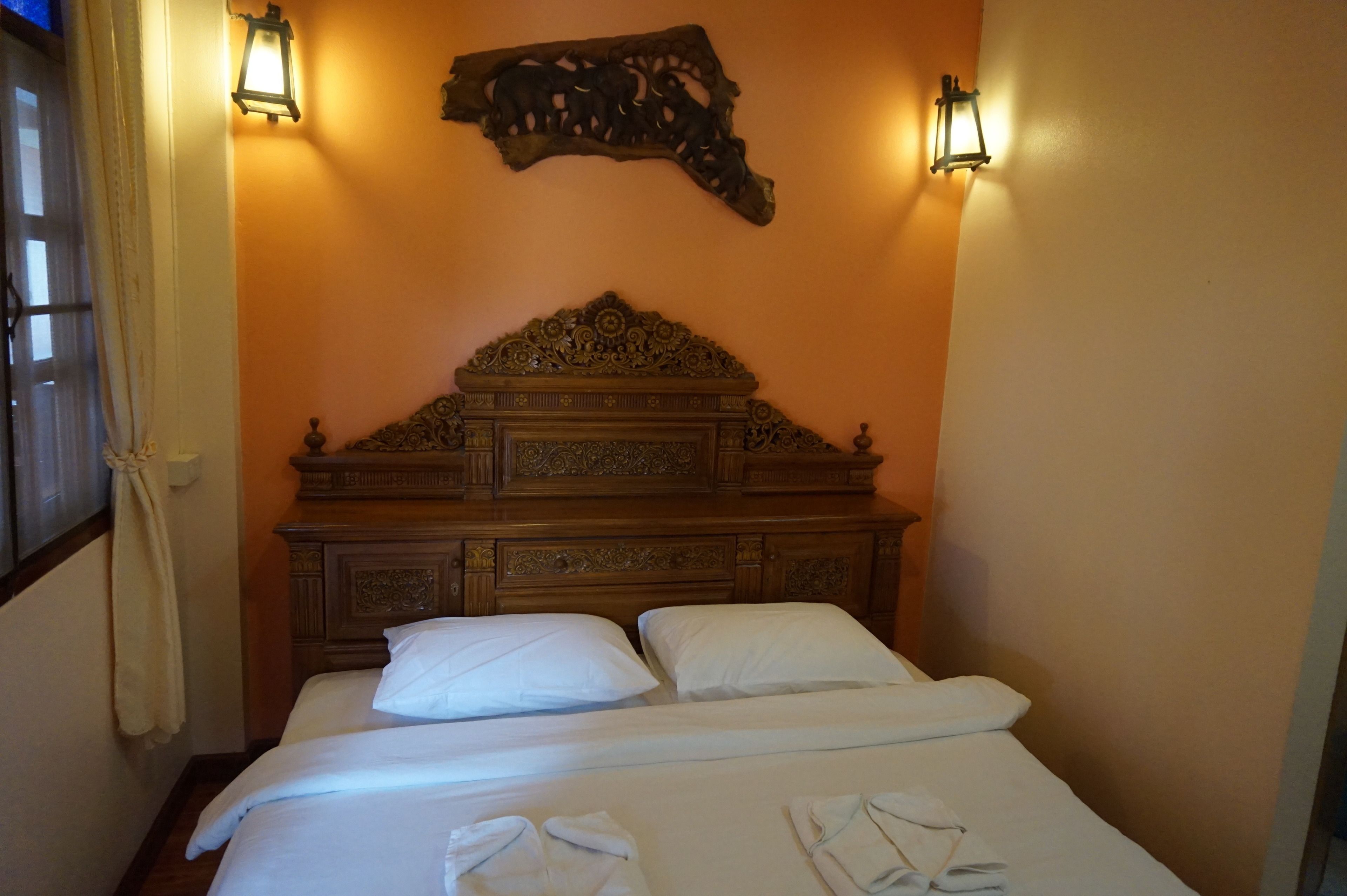 Habitación de hotel con cabecera de madera, dos almohadas blancas y toallas dobladas con cuidado sobre la cama.
