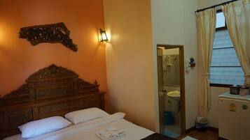 A hotel room with a wooden headboard, a bed with white linens, a wall-mounted light fixture, a mirror, and a window with curtains.