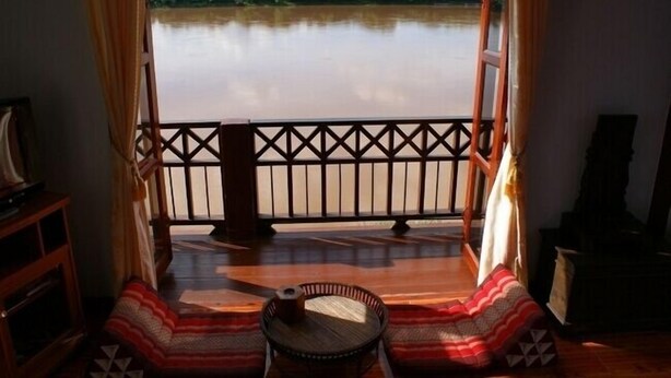 Een kamer met balkon en uitzicht op een rustige rivier, een houten vloer en een klein tafeltje met een kleed.