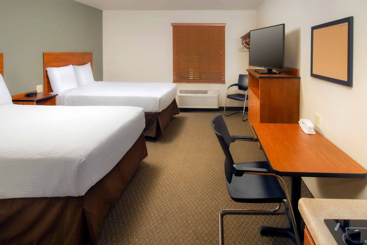 Ein Hotelzimmer mit zwei Betten, einem Schreibtisch, einem Stuhl, einem Fernseher und einer Klimaanlage.