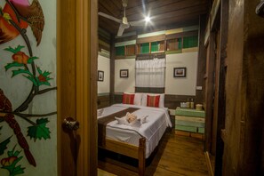 Una habitación con estructura de madera, dos camas, un ventilador de techo y un mural de aves en la pared.