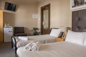 Quarto de hotel com duas camas, uma mesa, uma cadeira, uma televisão e uma porta.