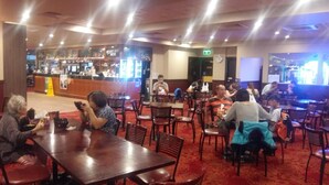 A restaurant with multiple tables and chairs, a bar area, and a clock on the wall. - Campsie Hotel (Campsie)