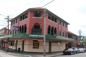 Um edifício vermelho com detalhes verdes e várias placas indicando que é um hotel.