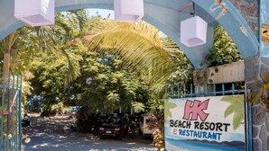 A beach resort entrance with a sign, palm trees, and parked cars. - HK Beach Resort (Moalboal)