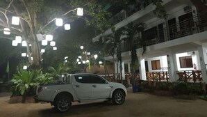 A white pickup truck parked in front of a building with multiple balconies and a tree with hanging lights. - HK Beach Resort (Moalboal)