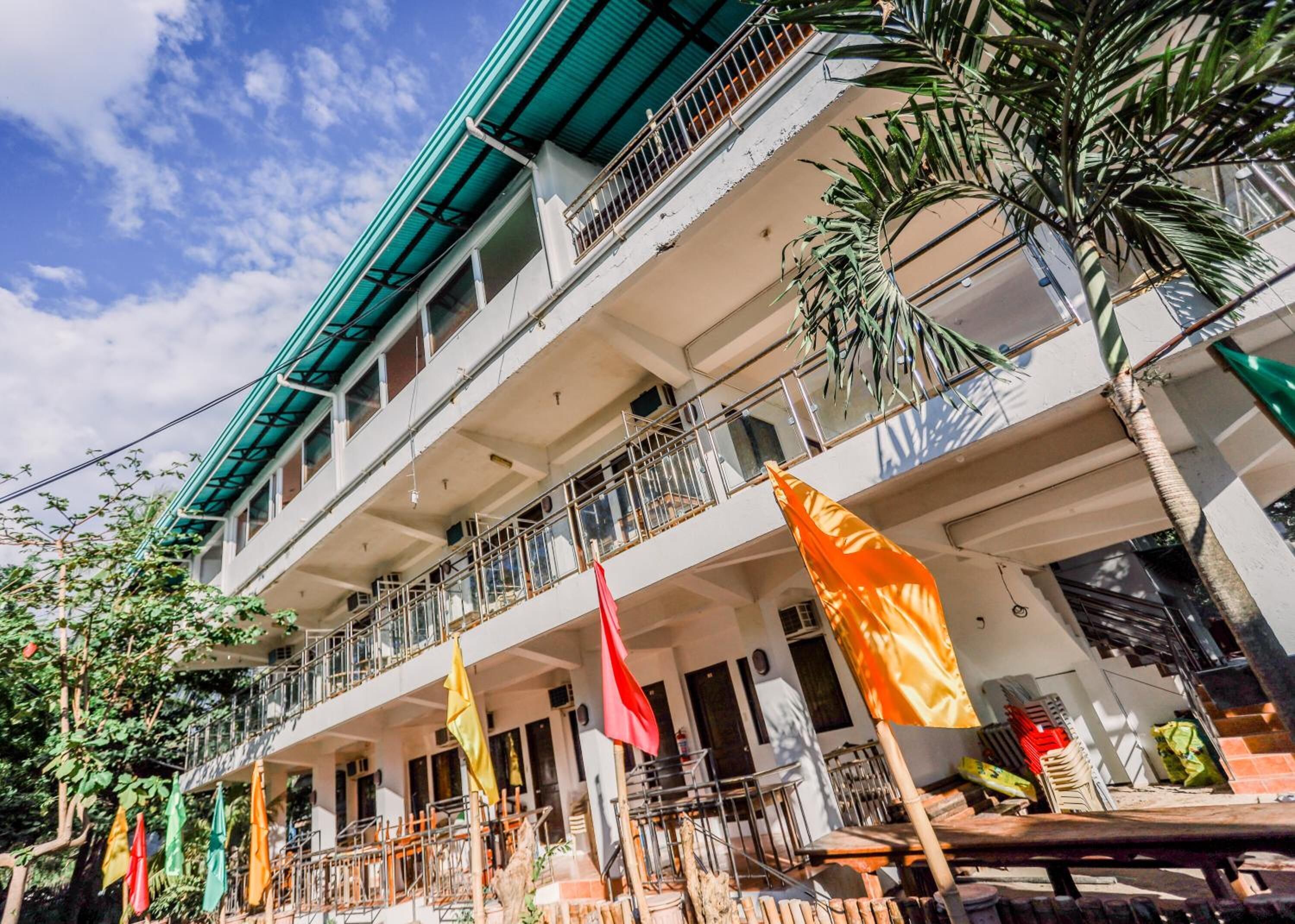 Een hotel met meerdere verdiepingen, balkons, terrasmeubels en een heldere lucht.