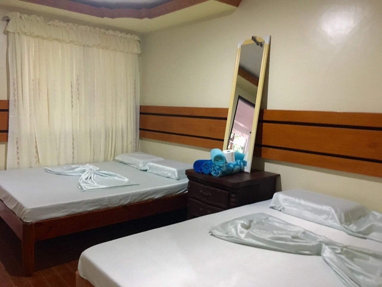Habitación de hotel con dos camas, cabecera de madera, espejo y cómoda con toallas y artículos de aseo.