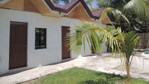 A two-story house with a white exterior and brown roof. There are two doors and windows, and a small garden area with palm trees. - Gorion Beach Resort (Samboan)
