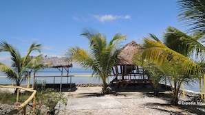 A beach scene with a thatched-roof structure, palm trees, and a clear blue sky. - Gorion Beach Resort (Samboan)