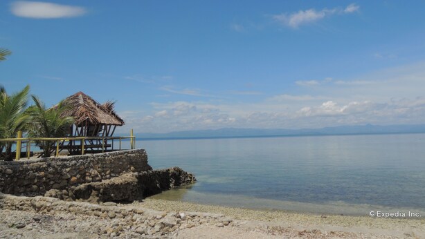 A beach with a thatched-roof hut, clear blue sky, calm water, and distant mountains. - Gorion Beach Resort (Samboan)