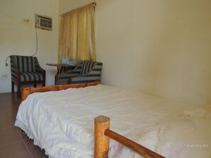 A room with a bed, two chairs, a small table, and a window with curtains.