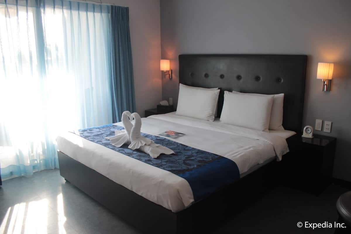 A hotel room with a large bed, a nightstand, a wall-mounted lamp, and a window with curtains.