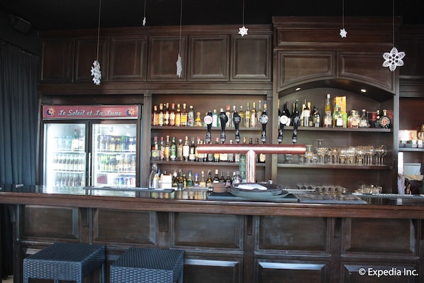 Eine Barbereich mit Holzausstattung, Regalen voller Flaschen, Gläsern und einer Kühlvitrine. Es gibt Hocker und eine Bar.