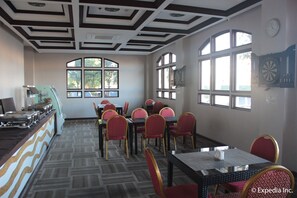 Un comedor con mesas y sillas, un área de cocina con estufa, y ventanas amplias con vistas a árboles.