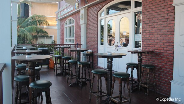 An outdoor seating area with multiple tables and stools, a brick wall, and a sign that reads "Cafe and Pub." - Sun Plaza Subic (Olongapo)