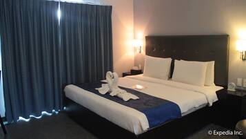 A hotel room with a large bed, a headboard, a nightstand, a lamp, and a curtain.